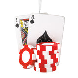 A novelty Christmas ornament shaped like a stack of red and white poker chips in front of two playing cards, specifically the Jack of Spades and an Ace of Spades, with a white hanging ribbon at the top, shown on a solid white background.