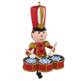 A festive toy soldier Christmas ornament playing a set of red drums with blue snowflake-patterned drumheads and gold trim, set against a plain white background.