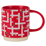 A red ceramic mug featuring a crossword puzzle design filled with holiday-themed words and small festive icons, with a beige speckled base and a red handle.